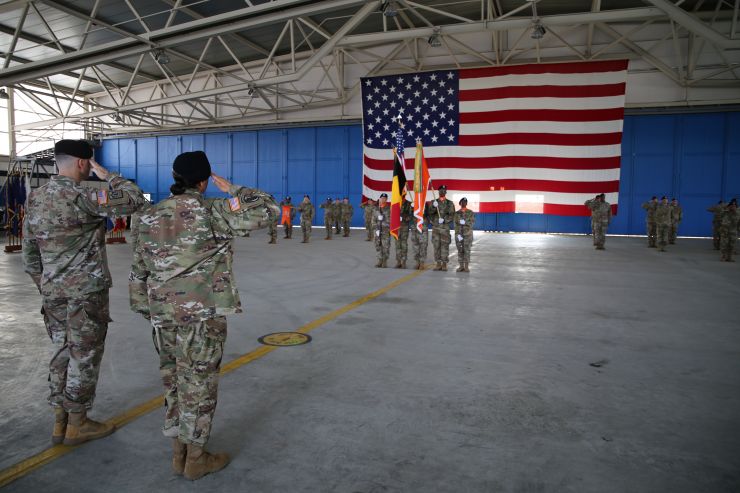 A photograph of two individuals saluting a large American flag at a ceremony